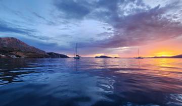 Sunset over the sea with sailboats and distant mountains.