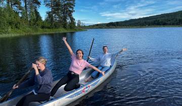 Three people canoeing on a lake with trees around.