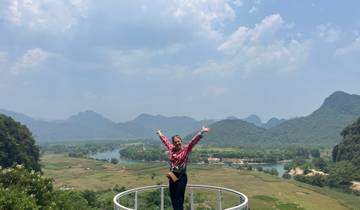 Person joyfully posing on an observation platform with a river and mountains in the background.