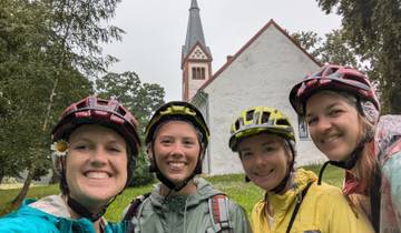 Four cyclists in front of a historic church on a rainy day.