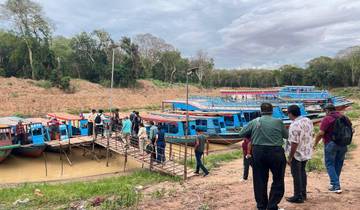 People boarding colorful boats at a riverbank, surrounded by lush greenery.