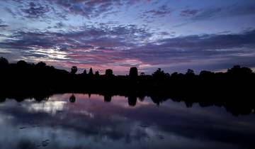 Silhouette of Angkor Wat reflected in water at sunset.