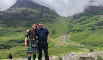 Two people posing in front of scenic hills with clouds.