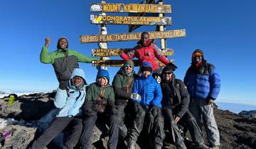 Group at the summit of Mount Kilimanjaro with a sign.