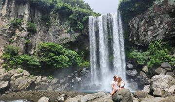 Couple sitting in front of a waterfall surrounded by greenery.