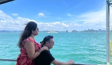 Couple on a boat enjoying a scenic view of the ocean with a cruise ship in the distance.