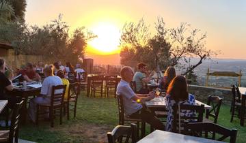 Open-air restaurant with people dining and watching the sunset over a hilly landscape.