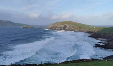 Coastal scene with waves crashing along a rugged shore and hills in the distance.