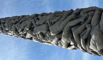 Monolith sculpture with figures intertwined, against a blue sky.