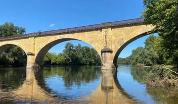 Stone bridge spanning over calm river waters amidst trees.