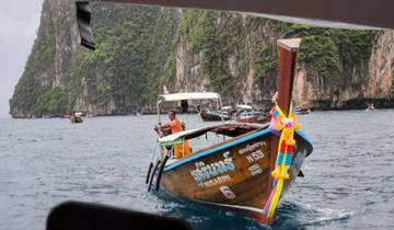 A wooden boat with a colorful decoration on the front sailing on the sea, with rocky cliffs in the background.
