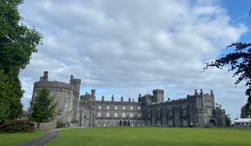 Imposing stone castle with bright green lawn and cloudy sky.