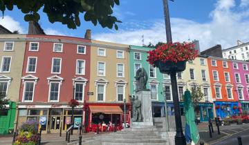 Row of colorful buildings in a city square with a statue and flowers.