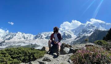 Person sitting on a rock with snow-capped mountains in the background.
