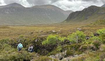 Two hikers in a vast green landscape with mountains.