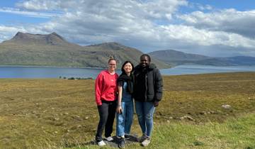 Three people posing with a scenic landscape of mountains and lake.