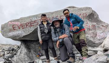 Three people posing with Everest Base Camp marker in a rocky area.