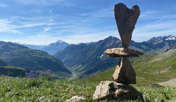 Balanced rock formation on top of a hill with mountains in the distant background.