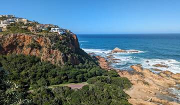 A scenic view of rocky coastline with waves crashing against the rocks, under a blue sky.