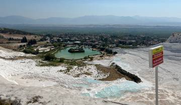Aerial view of Pamukkale terraced limestone formations with pools and a distant city view.
