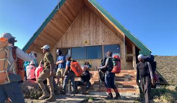 People gathered outside a wooden hut at a mountain base.