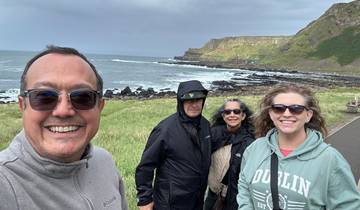 Group of people standing along a coastal path in windy weather.