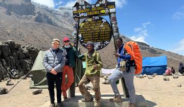 People posing under the Kilimanjaro National Park sign.