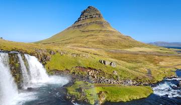 Waterfall beside a cone-shaped mountain with a slight rainbow.
