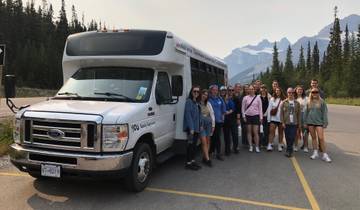 Group of people posing in front of a tour bus with snowy mountains in the background.