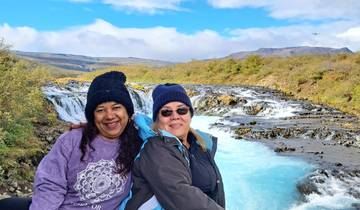 Two people smiling in front of a scenic waterfall.