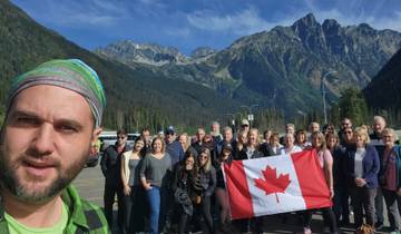 A large group of people posing in front of a mountainous landscape with a Canadian flag.