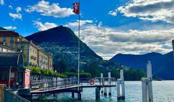 Lugano lake with mountains, a Swiss flag, and pier in the foreground.