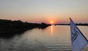 Sunset over a river with a boat and flag in the foreground.