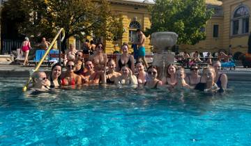 Large group in a pool posing for a photo, with a historic building facade in the background.
