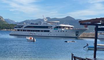 Large yacht moored in a harbor with mountains in the background.