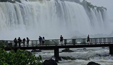 People walking on a viewing platform in front of a large waterfall.