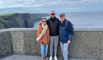 Three people standing on a cliff overlooking the ocean