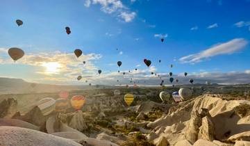 Hot air balloons flying over Cappadocia during sunrise.