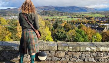 Person in a kilt overlooking a town with a valley view.