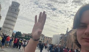 A person posing near the Leaning Tower of Pisa with a crowd around.