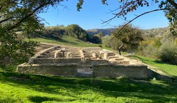 Archaeological ruins in a green hilly landscape under clear blue skies.