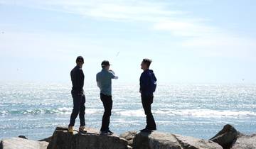 Three people standing on rocks by the ocean during the day.