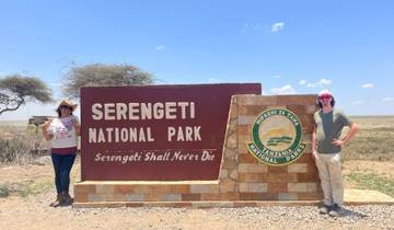 Two people standing by the Serengeti National Park sign.