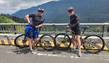 Two cyclists posing with their bikes on a bridge with mountains.