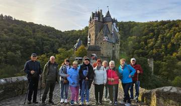 Group of tourists in front of a medieval castle surrounded by forest.