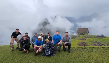 Group of people posing on a grassy hill in the clouds.