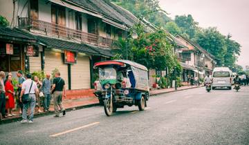 City street with a tuk-tuk and pedestrians.
