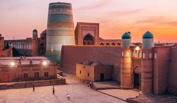 People walking in front of Khiva's iconic minaret and city walls at sunset.