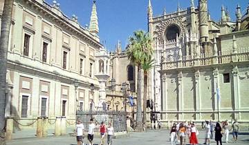 People walking near the Seville Cathedral with palm trees.