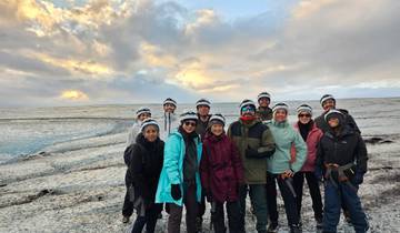 Group of people with helmets standing on a glacier under a cloudy sky.